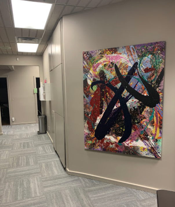The image shows an abstract art piece hanging on a wall inside an office space.