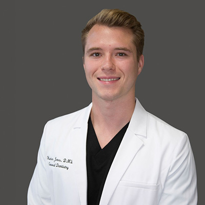 A young man wearing a white lab coat, smiling at the camera.