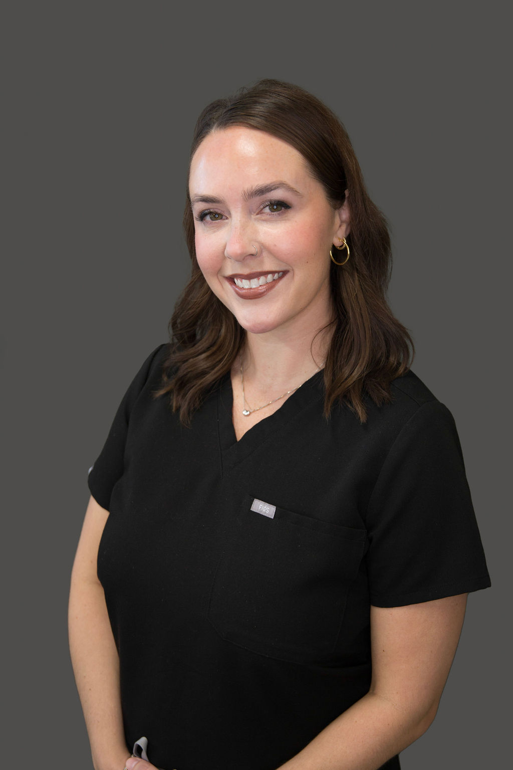 The image shows a woman wearing a black uniform with a white name tag, standing against a neutral background.