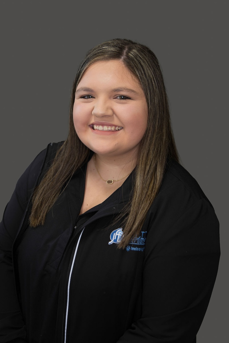 A young woman with a smile posing for a portrait against a grey background.