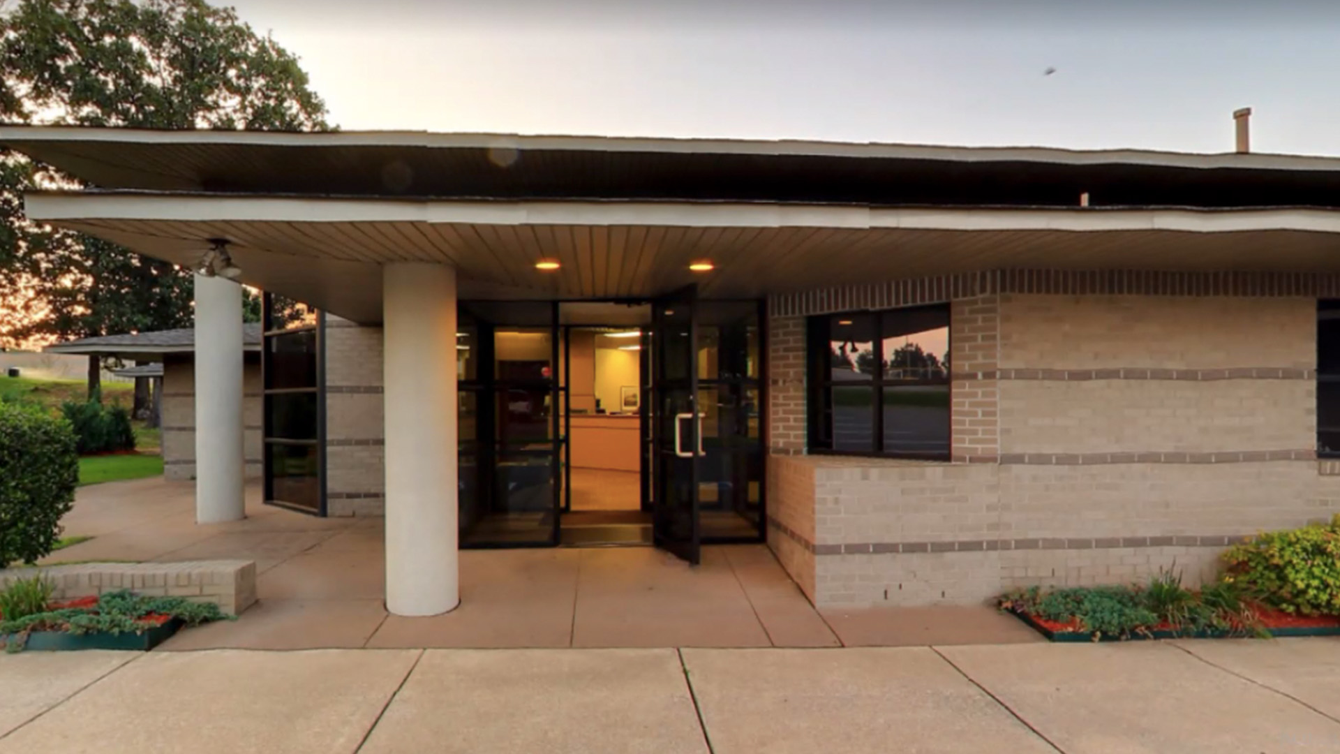 The image shows a single-story building with a covered entrance, featuring a flat roof and a brick facade.