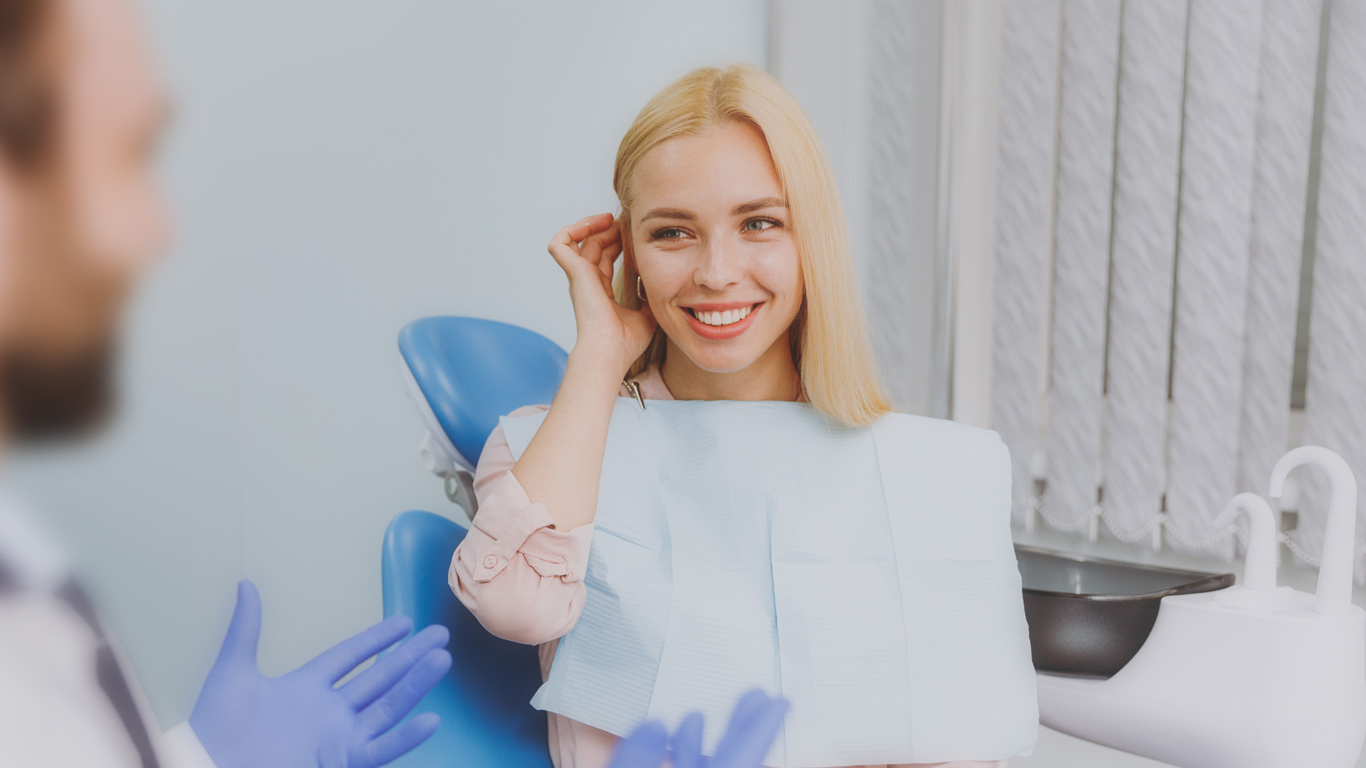 A woman with blonde hair sitting in a dental chair during a dental appointment, smiling at the camera.