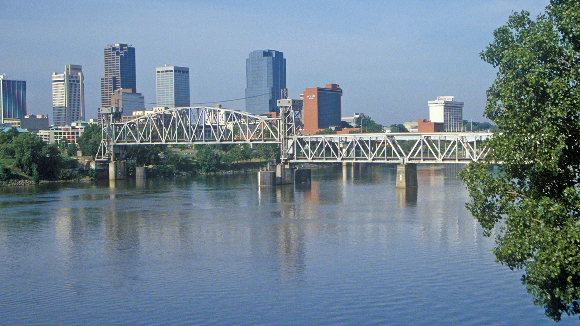 The image shows a city skyline with a bridge crossing over a river, featuring a clear blue sky in the background.