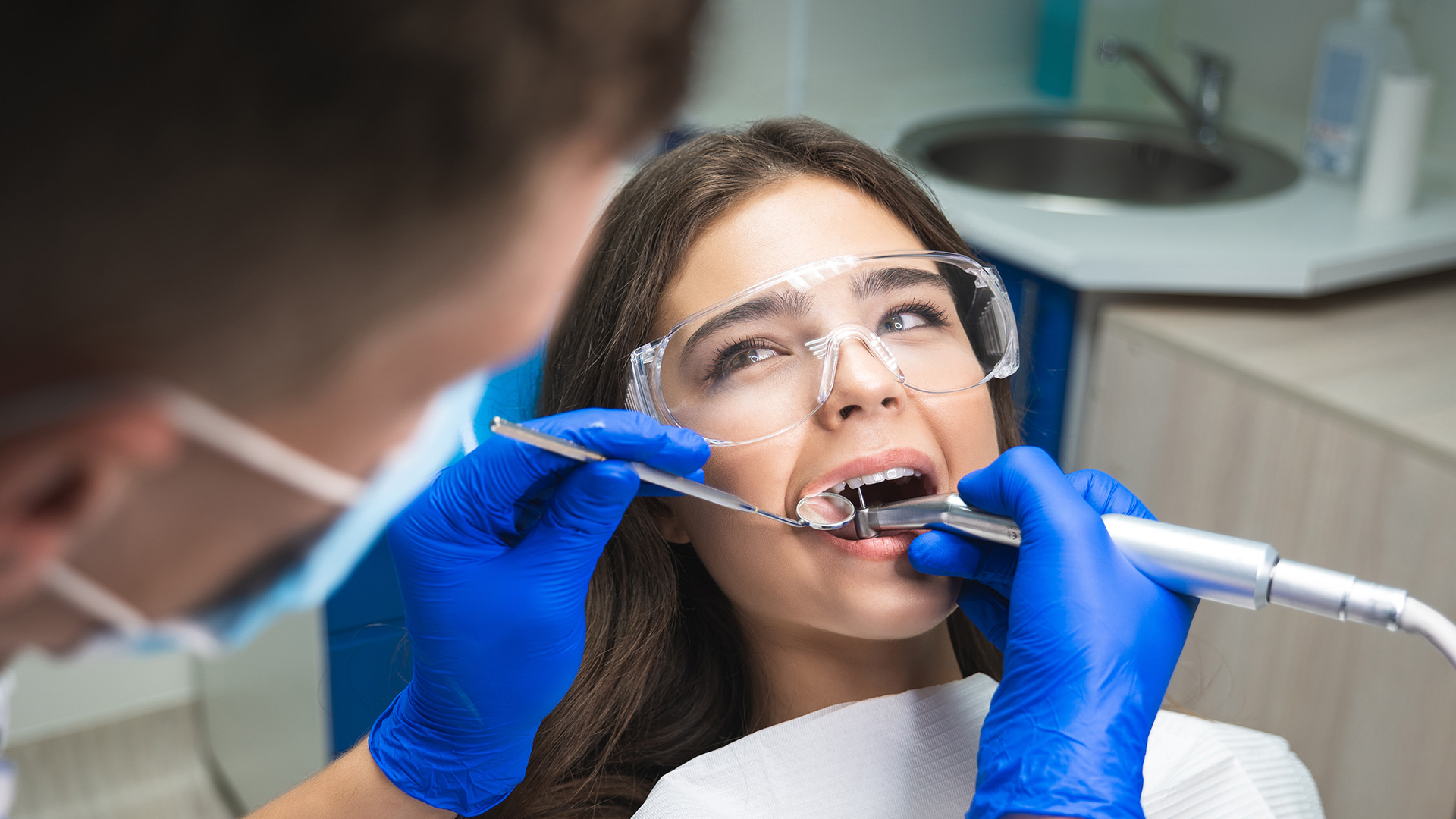 A dental professional performing a procedure on a patient s teeth with visible equipment and protective gear.