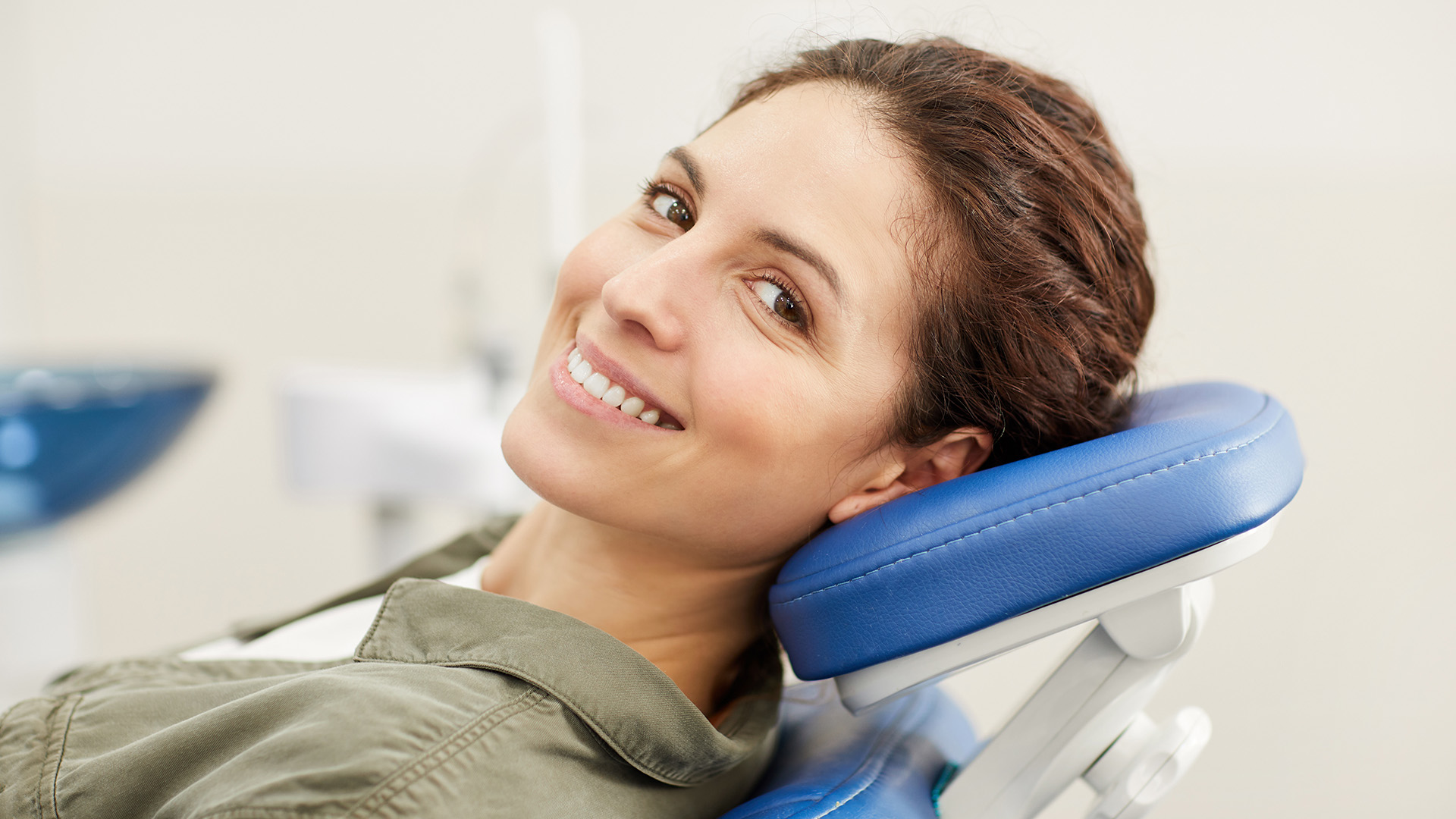 A woman wearing a military uniform sits in a dental chair with a bright smile, looking directly at the camera.