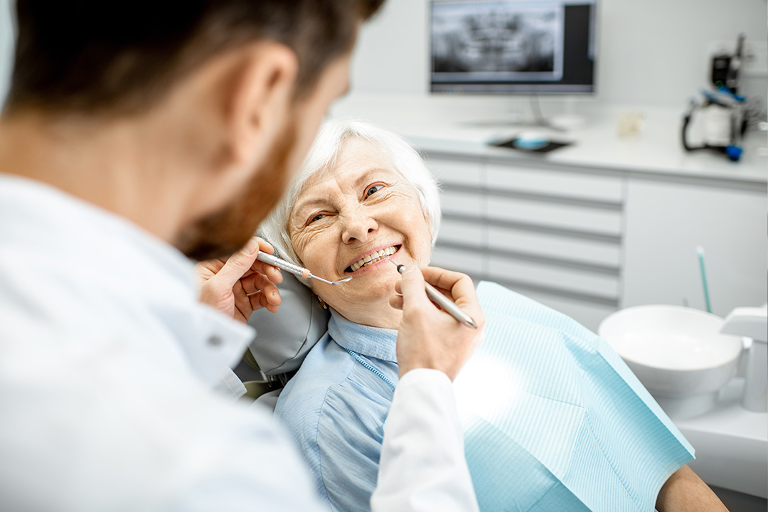 The image depicts a dental professional performing an examination on an elderly patient in a dental office setting.