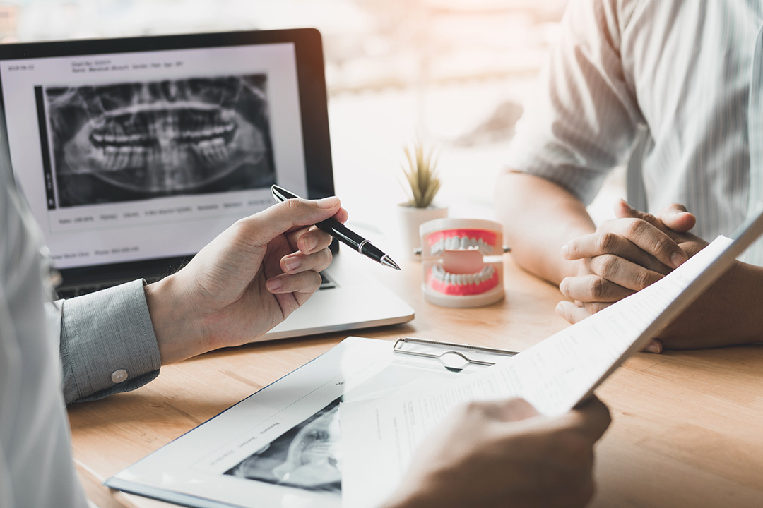 This is a split-screen photograph showing a dental professional on the left side of the screen engaged with a patient s medical records, while on the right, another dental professional appears to be reviewing digital X-rays and notes, with a patient seated at a desk looking over paperwork, both in an office setting.