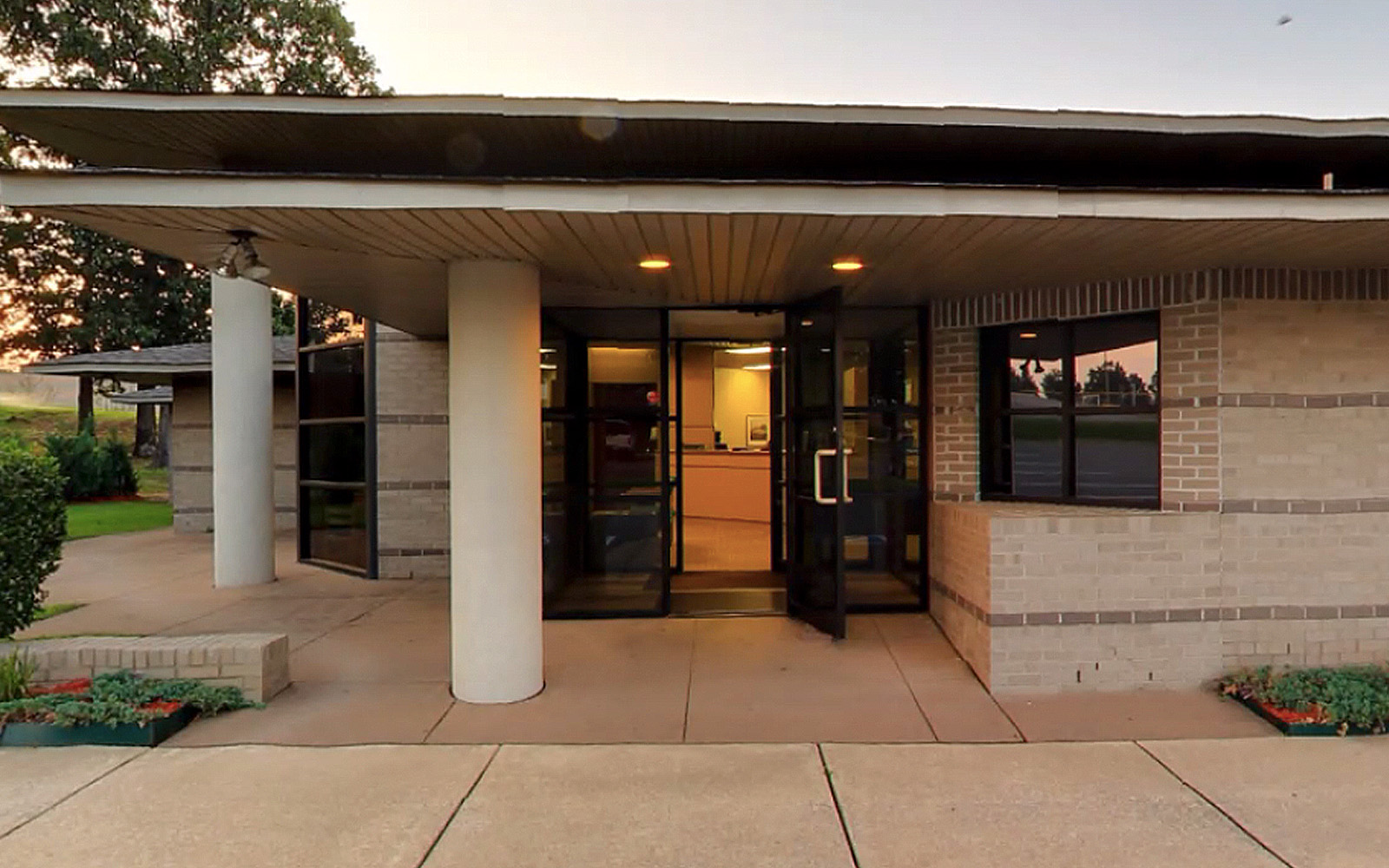The image shows the exterior of a building with a covered entrance, featuring a glass door and a brick facade.