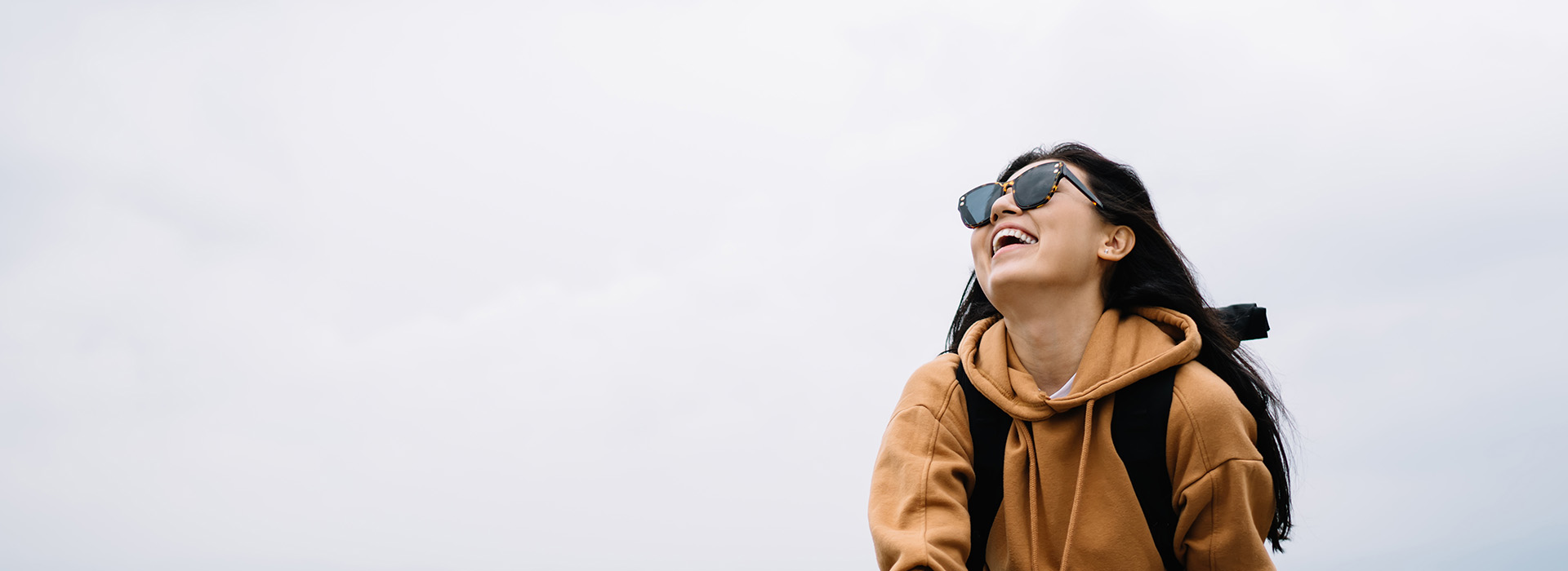 A person wearing sunglasses stands outdoors with a clear sky background, smiling and looking away from the camera.