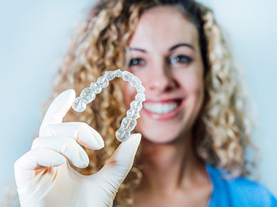 A woman wearing gloves holds up a transparent dental implant with a smile.