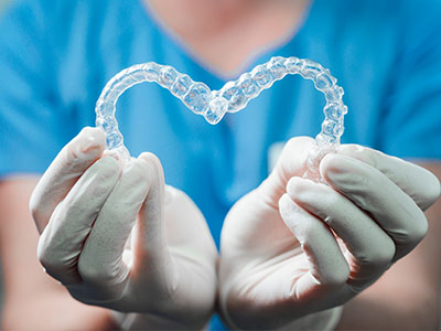 A dental professional s hands holding a heart-shaped clear aligner with transparent brackets, suggesting orthodontic treatment.