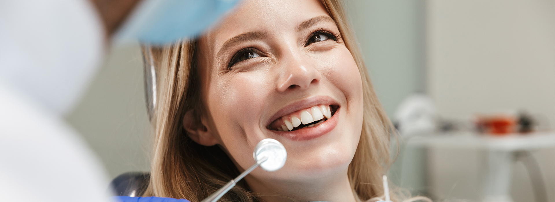 A woman with blonde hair smiling at a camera while seated in a dental chair during a dental appointment.