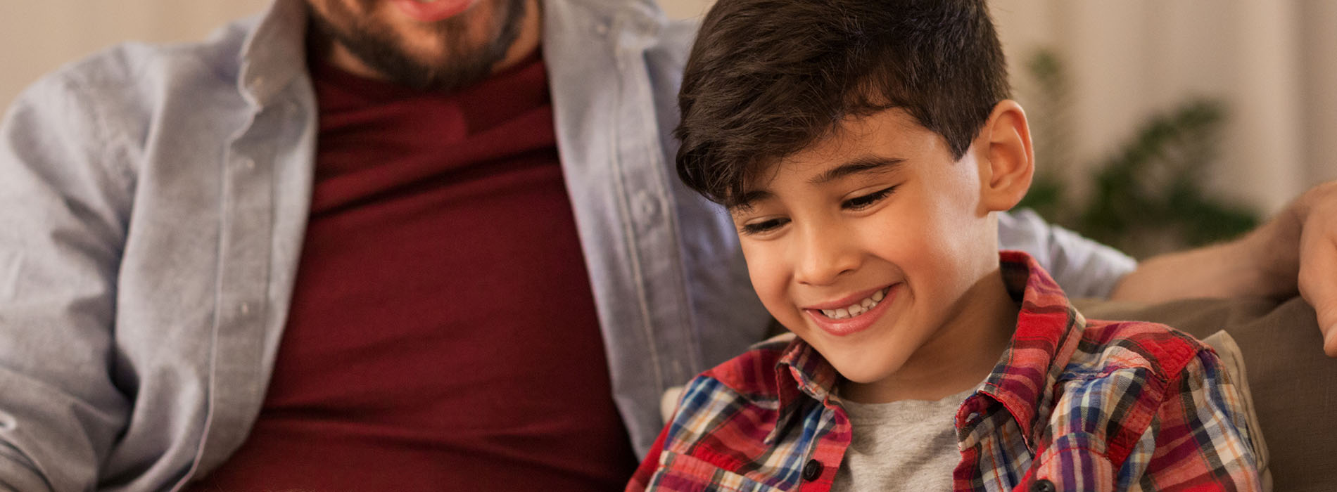 The image shows a man and a young boy sitting together on a couch, smiling at each other.