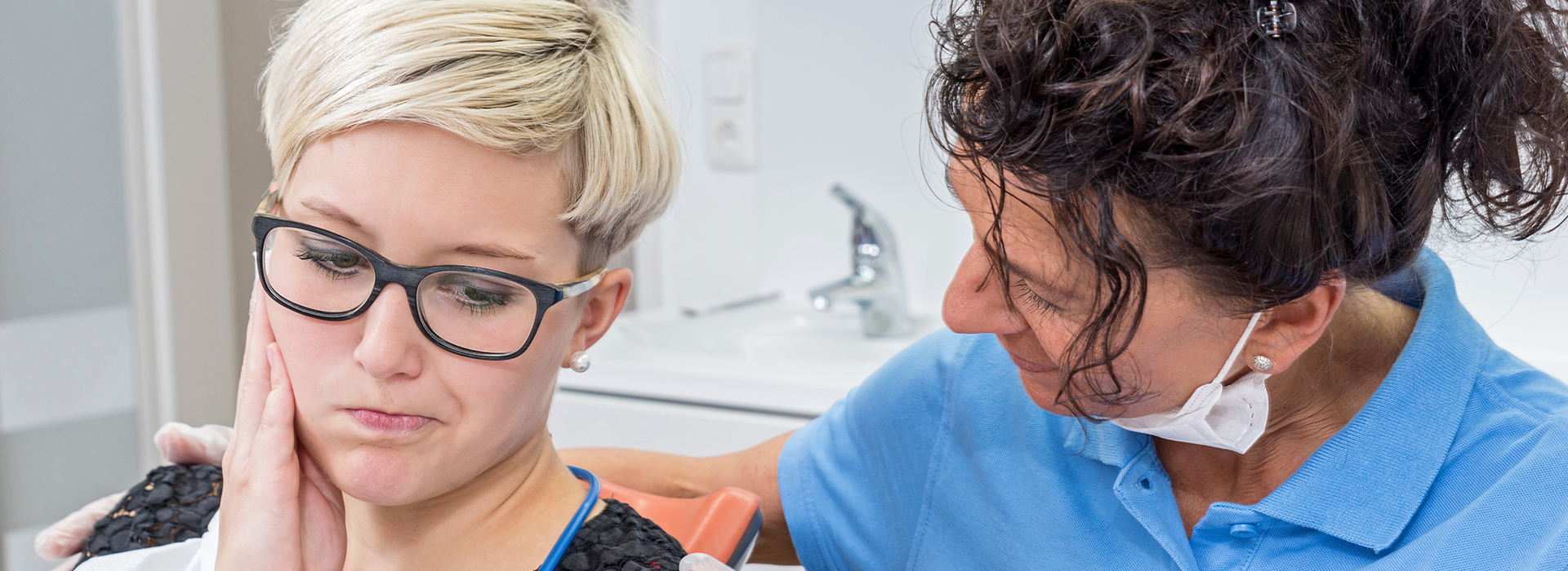 The image shows two individuals engaged in a dental care setting, where one person appears to be receiving dental treatment from another who is likely a dentist or dental hygienist.