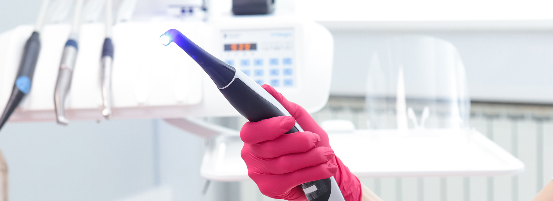 A person holding a blue device while wearing pink gloves and standing near medical equipment.
