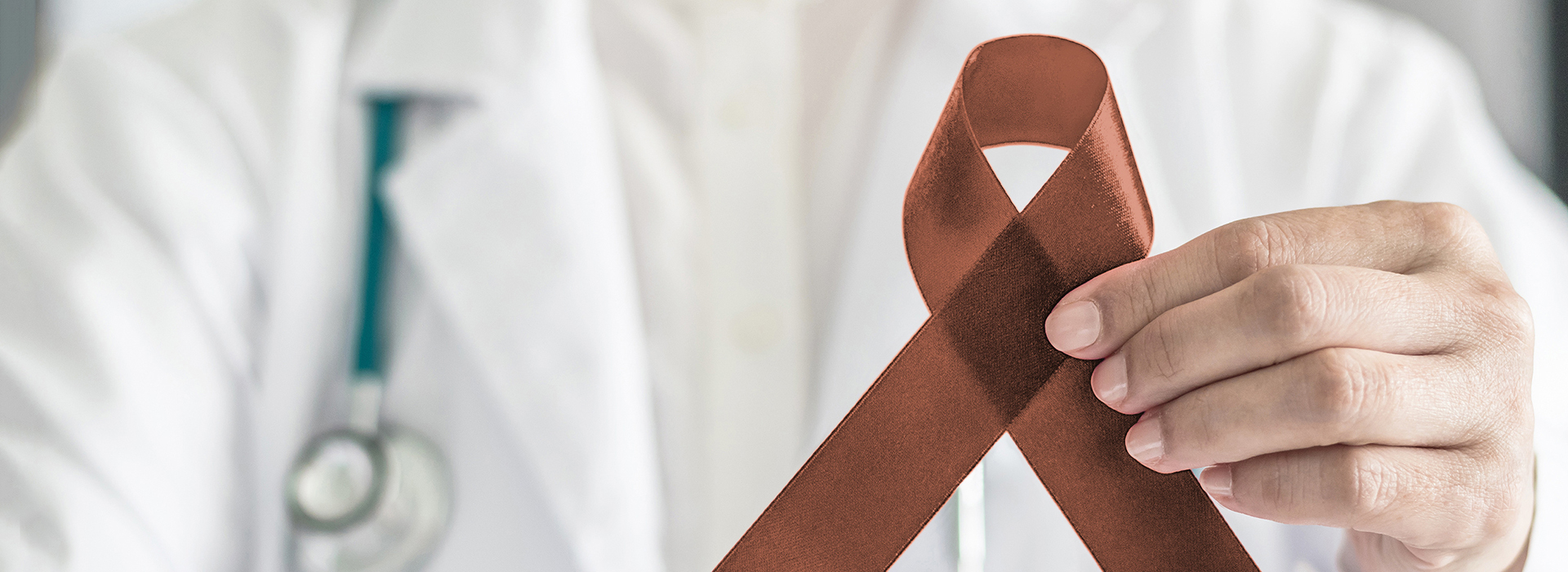 The image features a healthcare professional holding a brown ribbon with a red symbol on it against a white background.