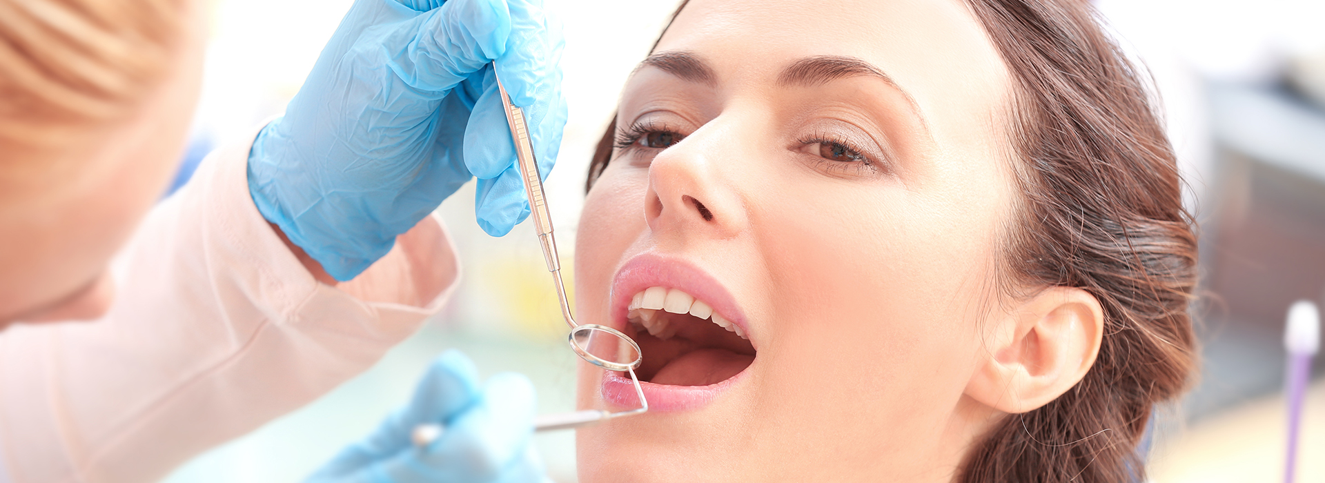 The image shows a woman receiving dental treatment, with a dentist performing a procedure on her teeth while she sits in a dental chair.