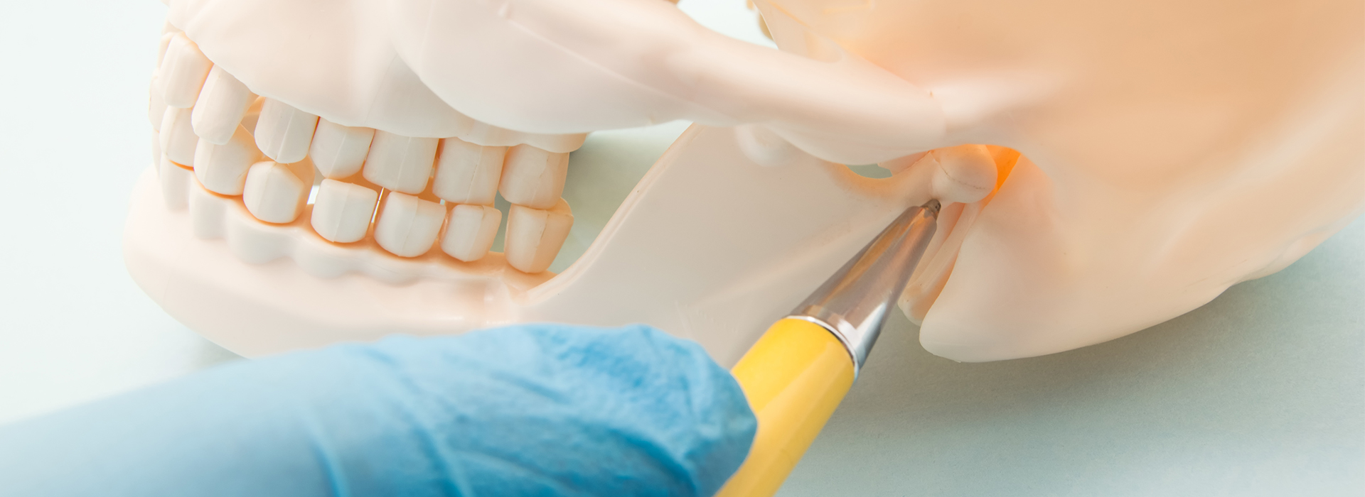 The image shows a close-up of a dental implant procedure with a focus on the surgical drill in action, set against a blurred background featuring medical equipment and a person s hand holding a tool.