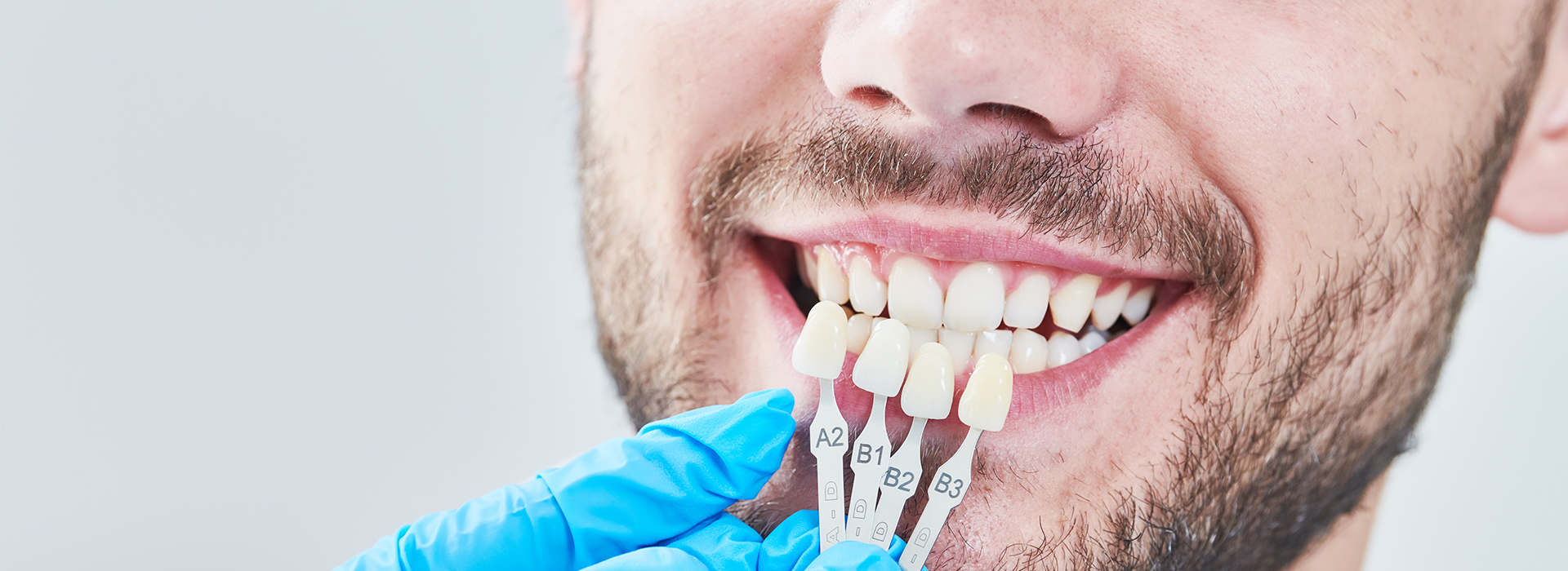 The image shows a man with a toothy smile looking at his teeth in a dental chair, with a device attached to his mouth.