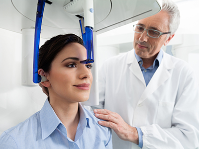 The image shows a woman seated in a dental chair with a blue headpiece, while a dentist stands beside her, both in a dental office setting.