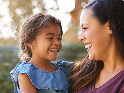 The image shows a woman with a young child, both smiling and looking at each other.
