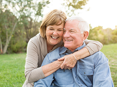 A man and woman, possibly an elderly couple, embracing each other outdoors during daylight.