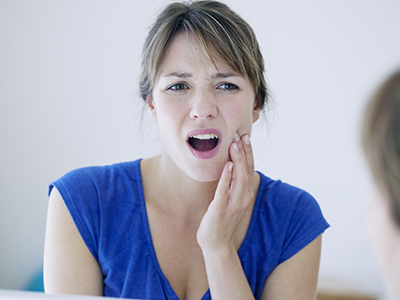 A woman with her mouth open appears surprised or concerned while looking at her reflection in a mirror.