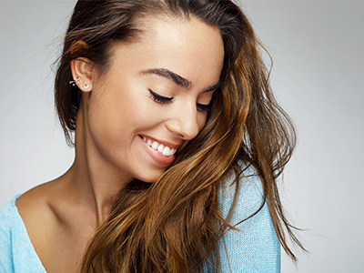 A woman with long brown hair smiles at the camera, looking over her shoulder with a relaxed expression.