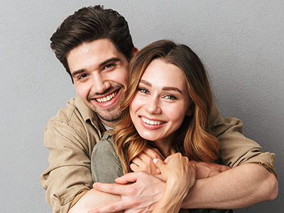 A man and woman are embracing each other with smiles on their faces, set against a neutral background.