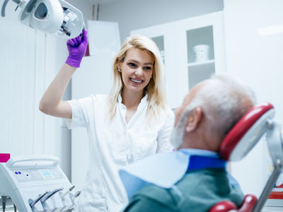 A dental hygienist assisting an elderly man in a dental chair with a smiling expression.