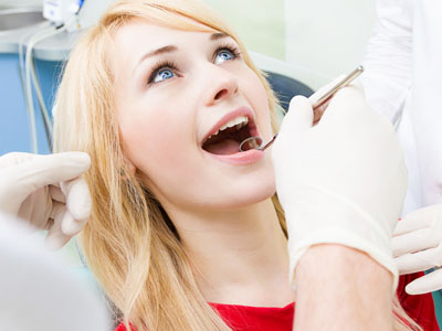 A woman receiving dental care with a wide-open mouth, while a dentist works on her teeth.