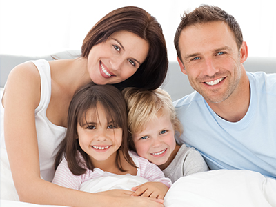 A family of four posing together on a bed with a happy expression.