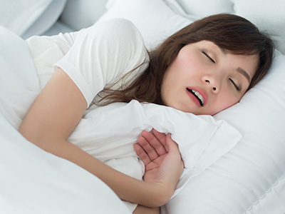 A woman sleeping on her side with her eyes closed, wearing a white t-shirt and holding a pillow over her chest.