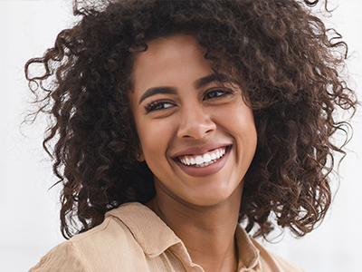 A smiling woman with curly hair, wearing a light-colored top, looking directly at the camera.