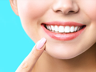 The image shows a close-up of a person smiling broadly with teeth, revealing a bright smile, against a light blue background.